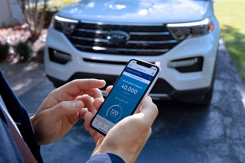 Closeup of a cell phone in a man's hand scheduling service in font of white Explorer® SUV